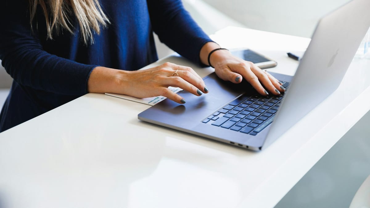 Woman writing on a laptop at a bright desk