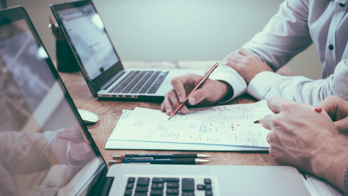 Person reviewing a plan with a pencil beside a laptop